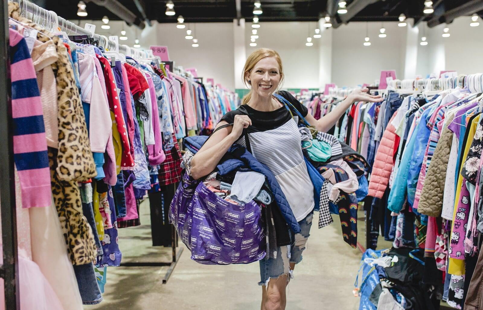 A young JBF shopper mom in a black Metallica T-shirt holds an outfit she intends to buy at her local JBF sale.