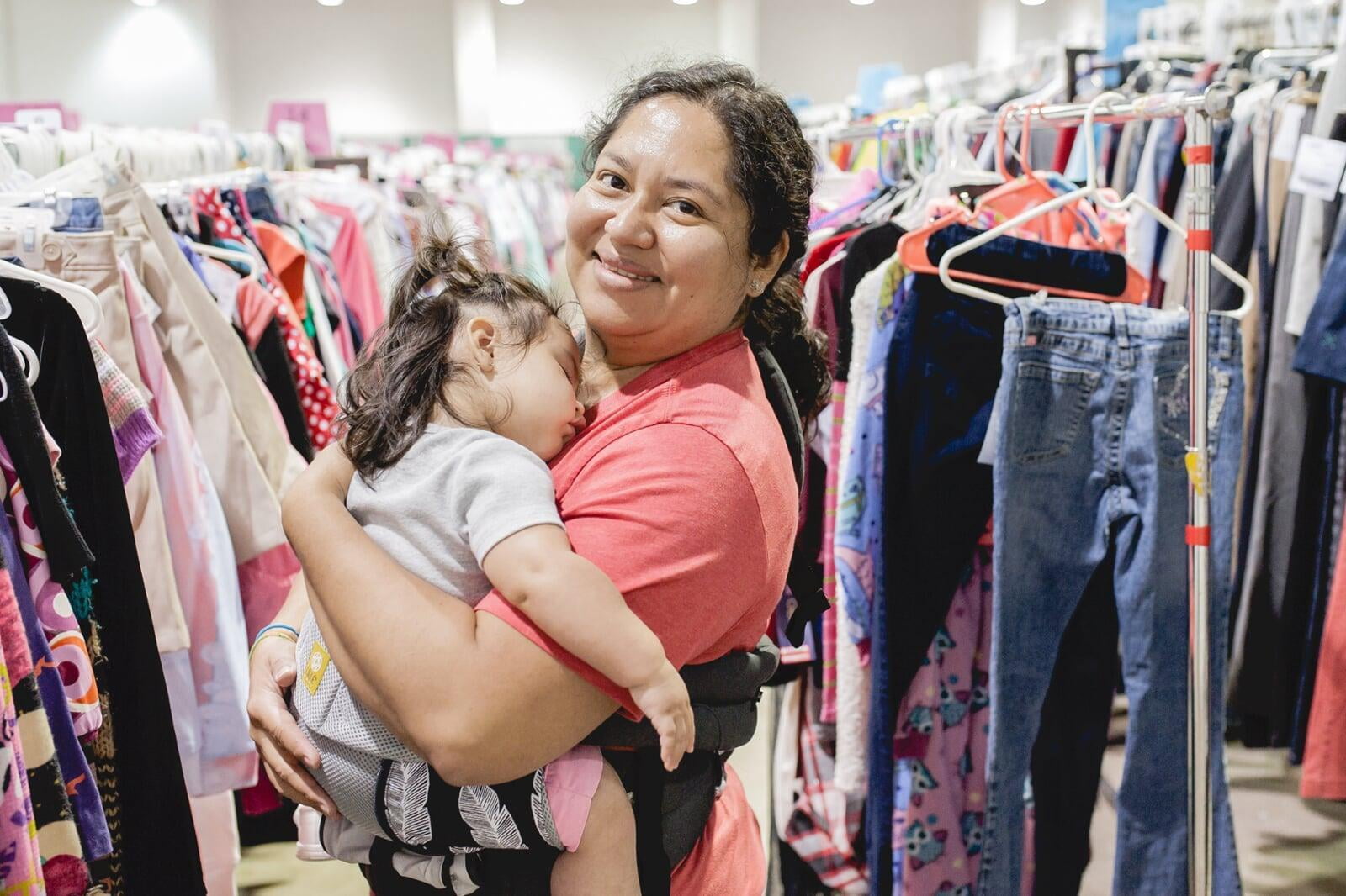 A mom holding her sleeping child while shopping for her daughter. 